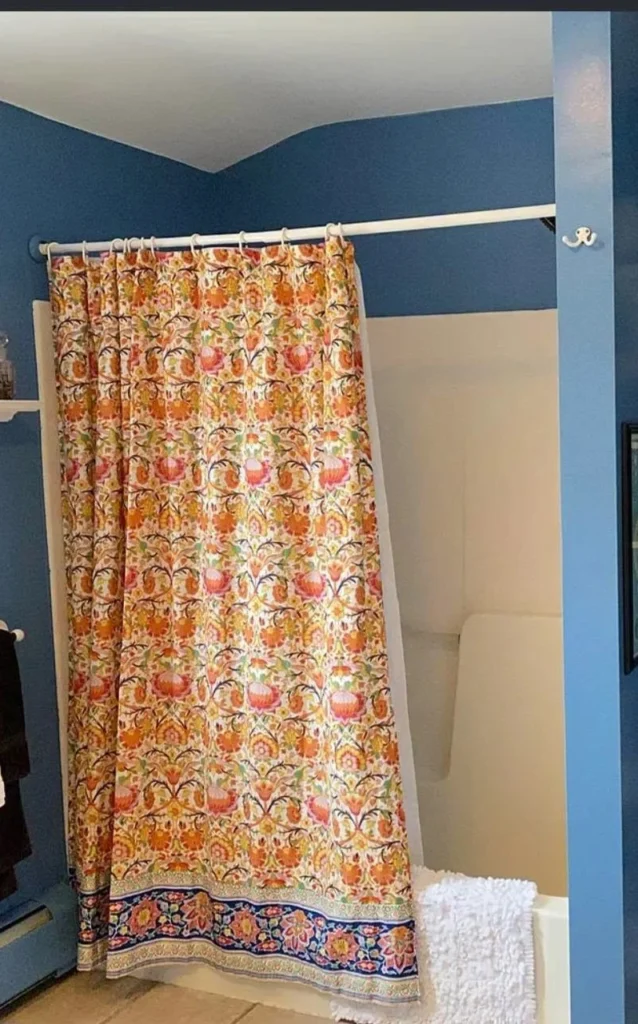 River Heights bathroom before renovation, with the original alcove bathtub behind a floral shower curtain and blue-painted walls